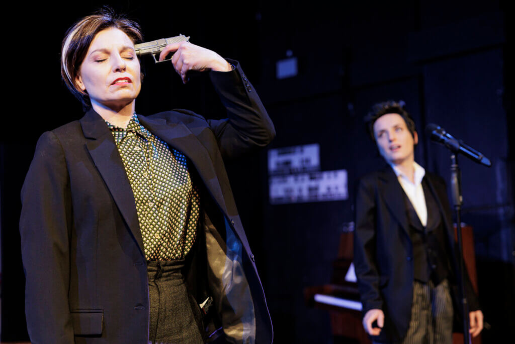 Claudia Lüftenegger steht als Margarete Faust vorne links und hält sich eine Pistole gegen die Schläfe.