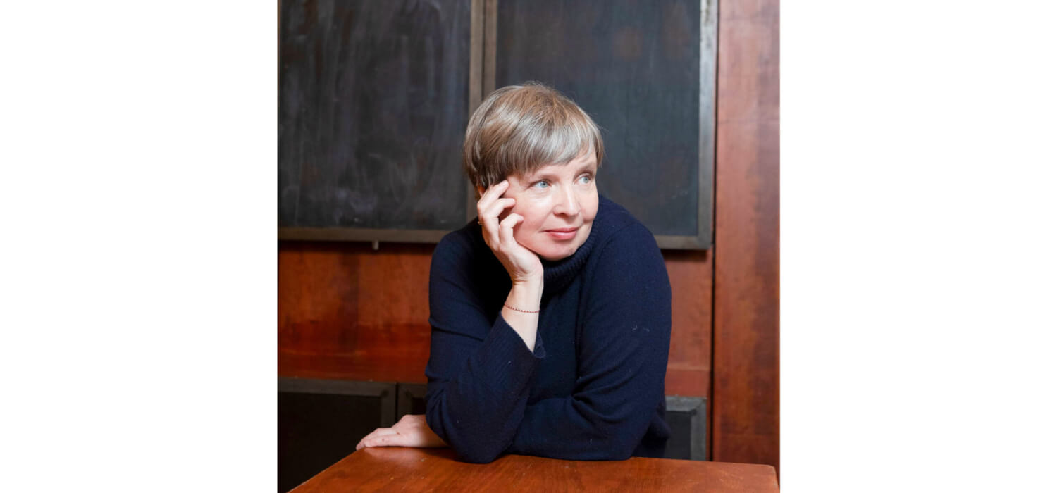 Jenny Erpenbeck steht an einem braunen Tisch.