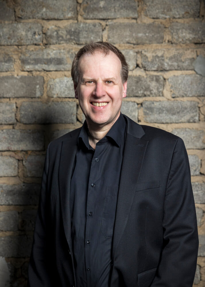 Porträt von Michael Steindl, Intendant Schauspiel am Theater Duisburg, vor einer Steinmauer.