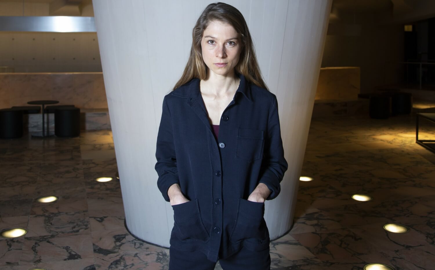 Schauspielerin und Autorin Lea Ruckpaul im Foyer des Düsseldorfer Schauspielhauses. Sie steht vor einer Betonsäule und hat die Hände in ihre Blusentaschen gesteckt.