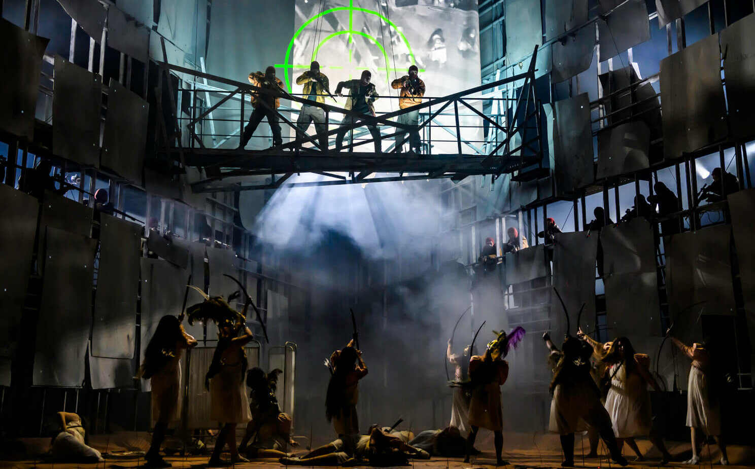 eine vernebelte Bühne mit bewaffneten Darstellern oben auf einer Brücke, die auf andere bewaffnete Figuren unten zielen