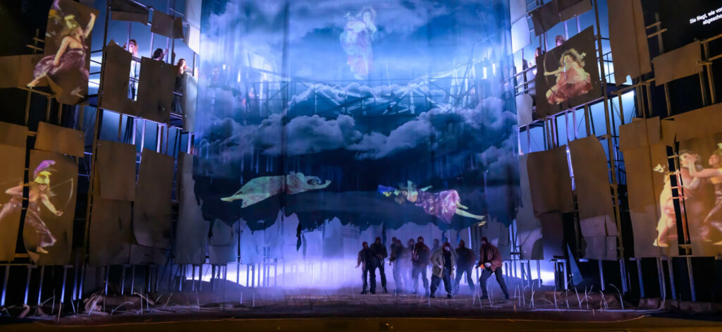 eine blau beleuchtete Bühne mit Olymp-Himmel und unten Kämpfer:innen
