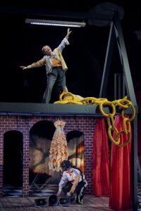 eine Bühne, auf einer Art Mauer eine Person mit ausgestreckten Armen