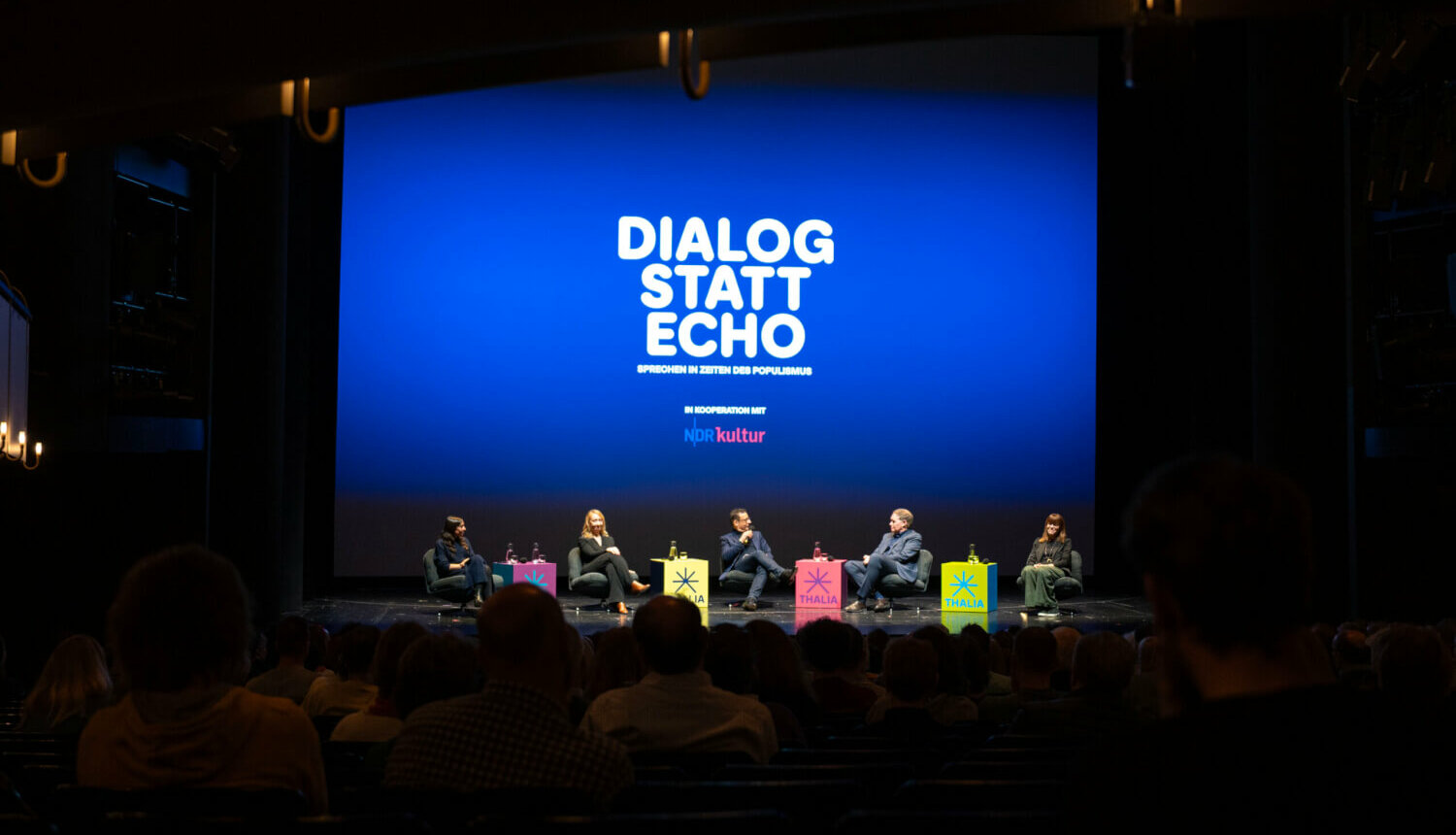 Zu sehen ist eine große Schrift DIALOG STATT ECHO, Sprechen in Zeiten des Populismus und fünf Personen, die in einer Reihe sitzen.