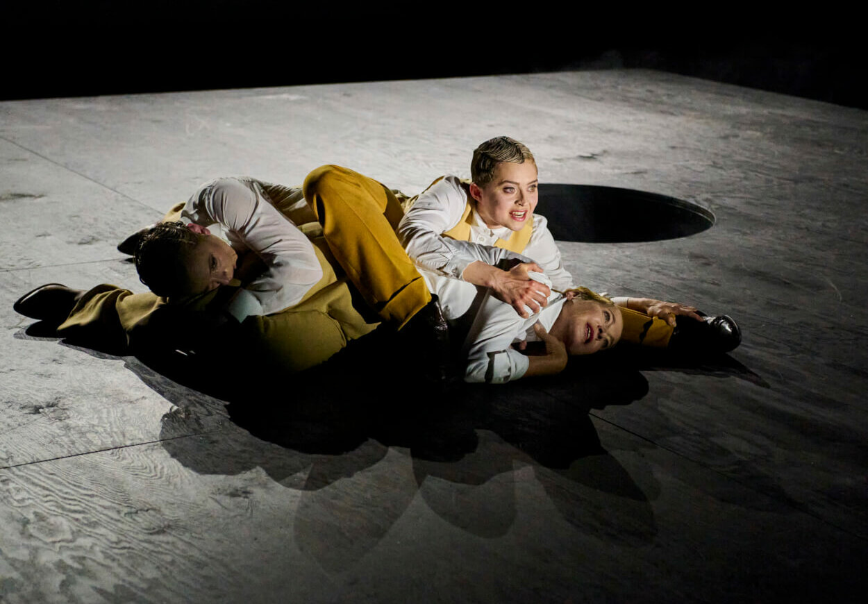 drei Personen in einem Knäuel auf einer schwach beleuchteten Bühne