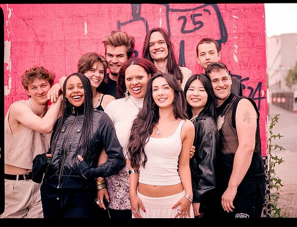 Jahrgang 2025 der Ausbildung für zeitgenössisches Theater an der Berliner Universität der Künste. Zehn Frauen und Männer stehen vor einer pink-roten Betonwand und strahlen in die Kamera.