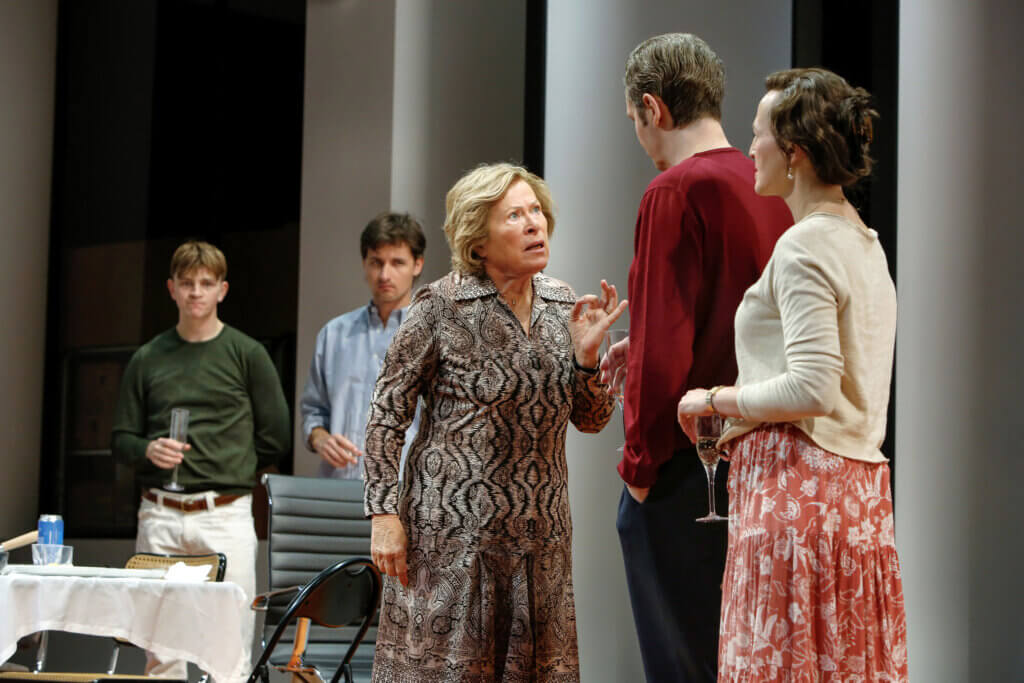 Merope konfrontiert Ödipus und erhebt mahnend ihre Hand. Er steht rechts mit dem Rücken zum Publikum, ihr zugewandt. Der Rest des Ensembles schaut den beiden zu.