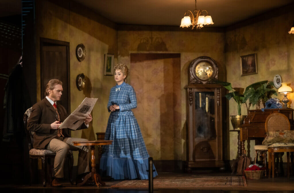 Ein historisches Wohnzimmer mit Standuhr, alter Deckenlampe und antiken Möbeln. Links befindet sich Ehepaar Bunting.