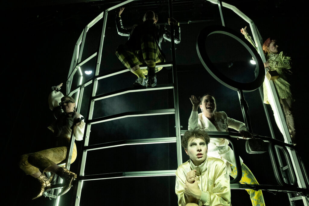 Das Ensemble hängt im viel bespielbaren Gerüst. Alles erscheint düster und bedrohohlich. Hardy Punzel sitzt vorne und blickt beklommen ins Publikum.