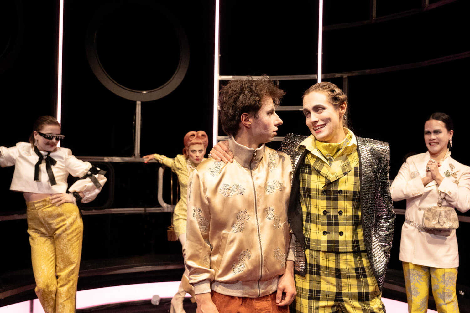 Das Ensemble lehnt im Hintergrund an das Metallgerüst. Vorne stehen Timm Thaler (Hardy Punzel) und Baron Lefuet (Simone Oswald). Lefuet legt den Arm um Thalers Schulter.