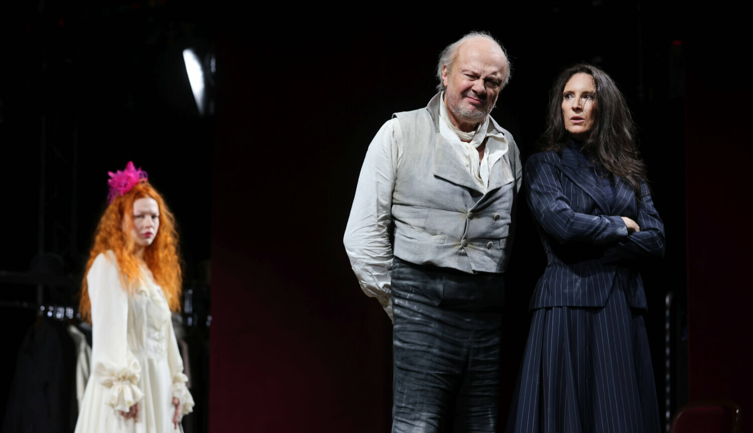 Juliette Larat steht als Dorka Dušková alias Dolly Delors im Hintergrund. Sie beobachtet Herbert Föttinger (Lorenzo da Ponte) und Maria Köstlinger (Nancy Krahl) wie sie vertraut eng beieinander stehen.