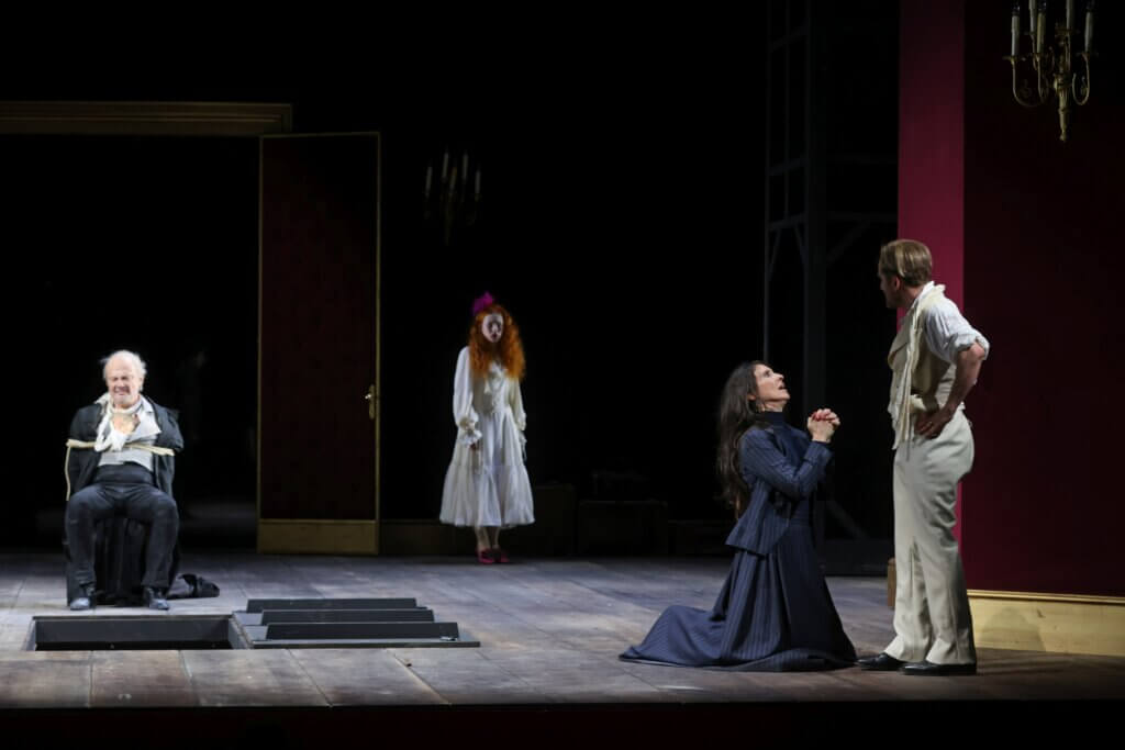 Lorenzo Da Ponte sitzt gefesselt auf einem Stuhl. Vor ihm ist eine Luke im Boden. Hinten steht Dorka Dušková bzw. Dolly Delors. Rechts kniet Nancy Krahl und fleht James N. Brodnik auf Knien an.