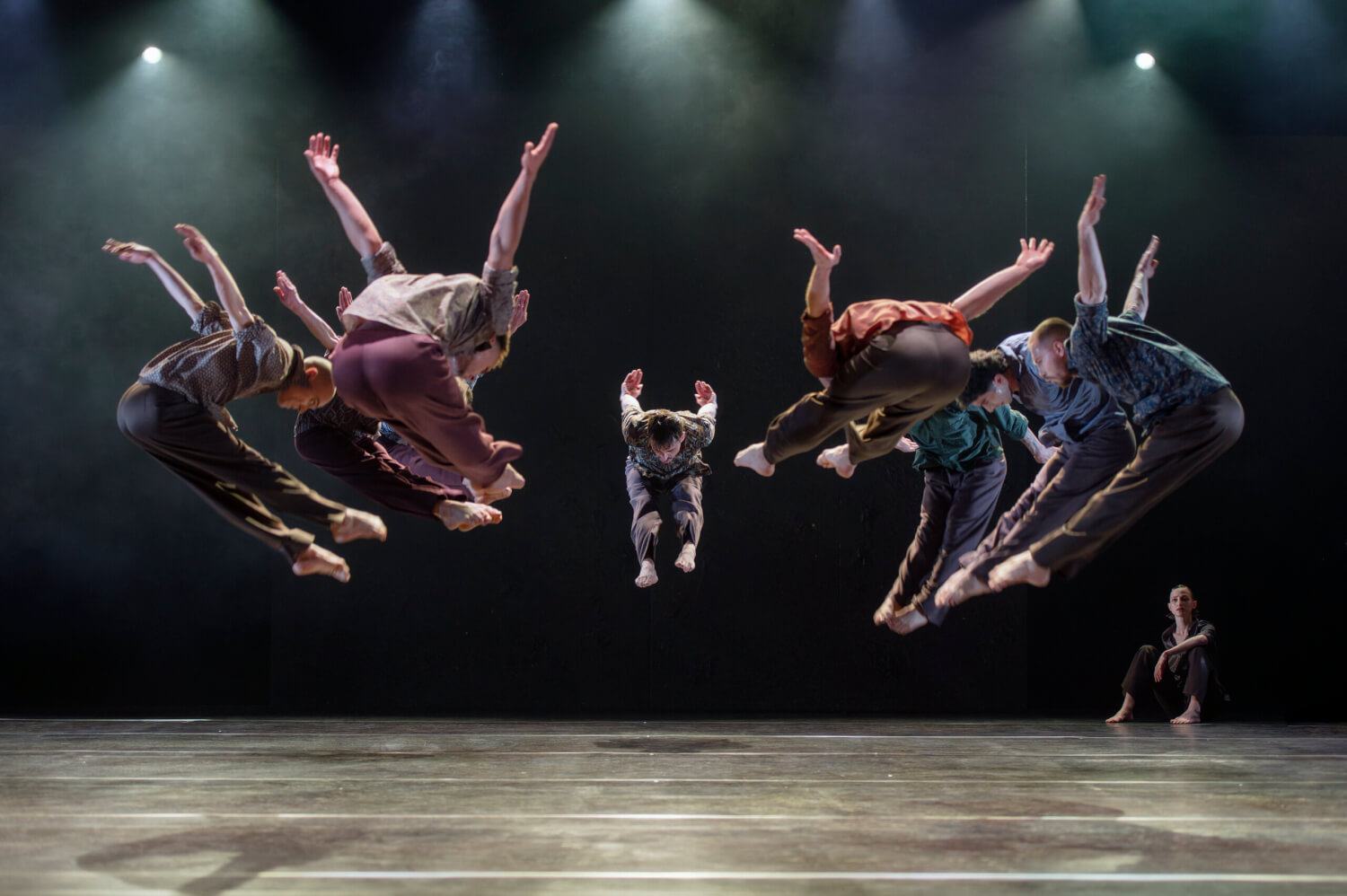 Aufführungsfoto von „Les Noces & Le Sacre du printemps“ von Didy Veldman und Ricardo Fernando am Staatstheater Augsburg. Acht Tänzer im Kreis springen synchron hoch, die Beine nach vorne gestreckt, die Arme nach hinten hoch gestreckt.