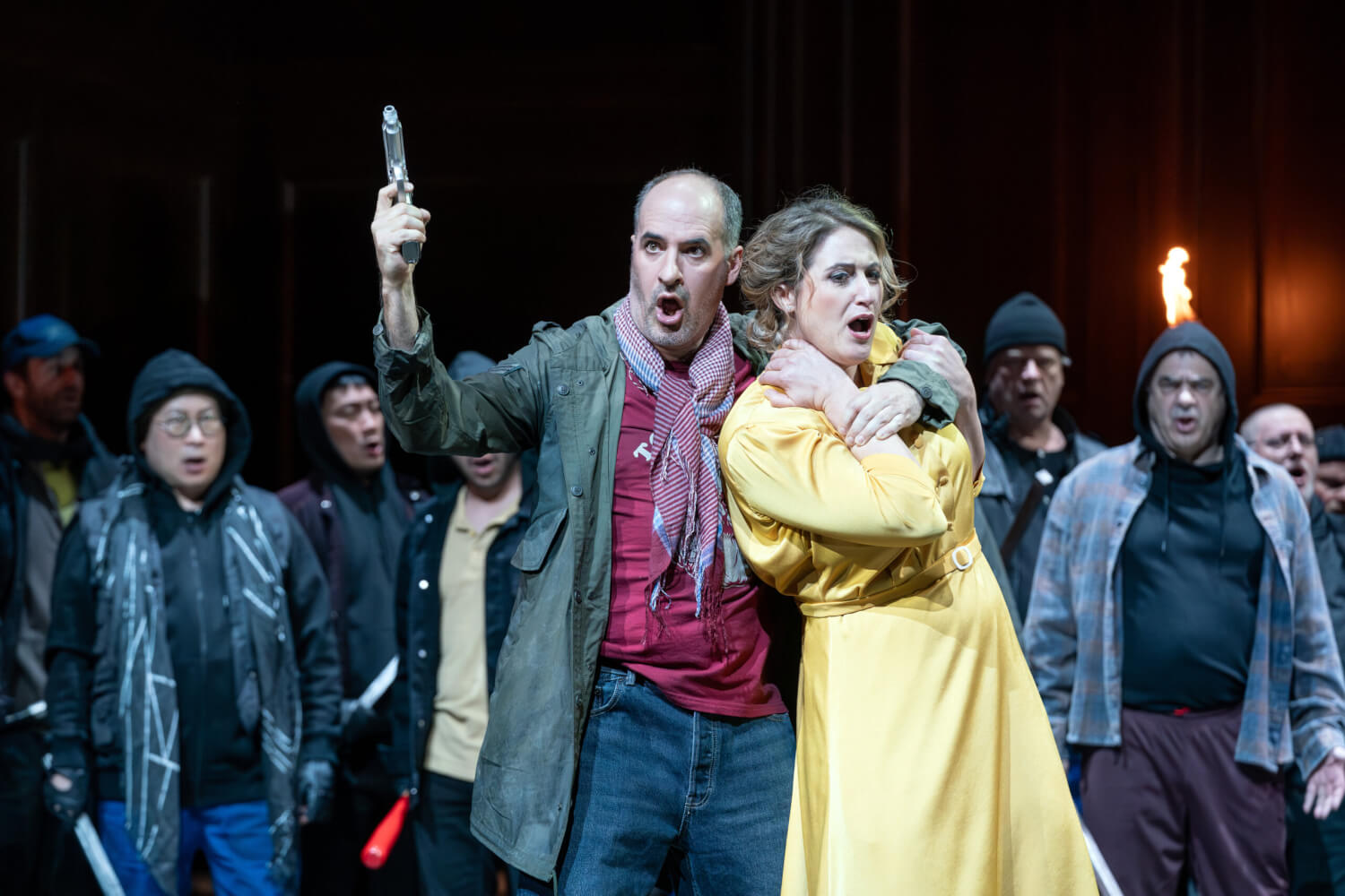 Aufführungsfoto von „Regina“ von Albert Lortzing an der Oper Leipzig. Eine Frau im gelben Kleid wird von einem Mann am Oberkörper festgehalten, während er eine Pistole in die Höhe hält.