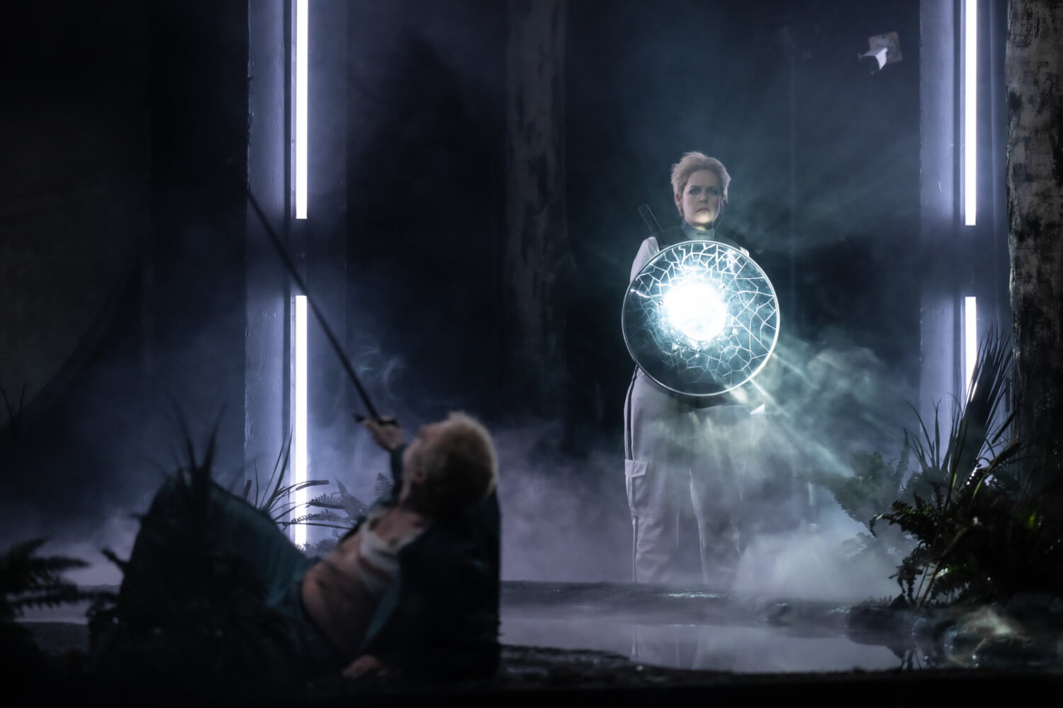 Daniel Johannson liegt vorne links im Schatten auf dem Bühnenboden und streckt sein Schwert in die Höhe. Hinten rechts steht Trine Møller mit einem hell leuchtenden Scheinwerfer, der nach vorne strahlt.