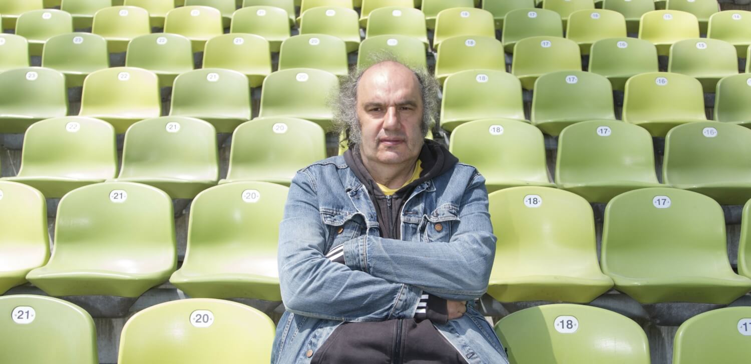 Matthias Lilienthal im Münchner Olympiastadion. Er sitzt auf einem Schalensitz auf der Tribüne und hat die Arme vor der Brust verschränkt.