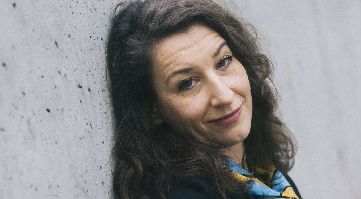 Tatjana Gürbaca in einem ruhigen Moment beim Titelshooting für die aktuelle Ausgabe der DEUTSCHEN BÜHNE in ihrer Heimatstadt Berlin. Sie lehnt an einer Betonwand und schaut seitlich in die Kamera.