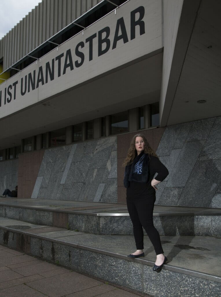 Lucia Lucas auf einer hohen Stufe vor einem Theatergebäude.