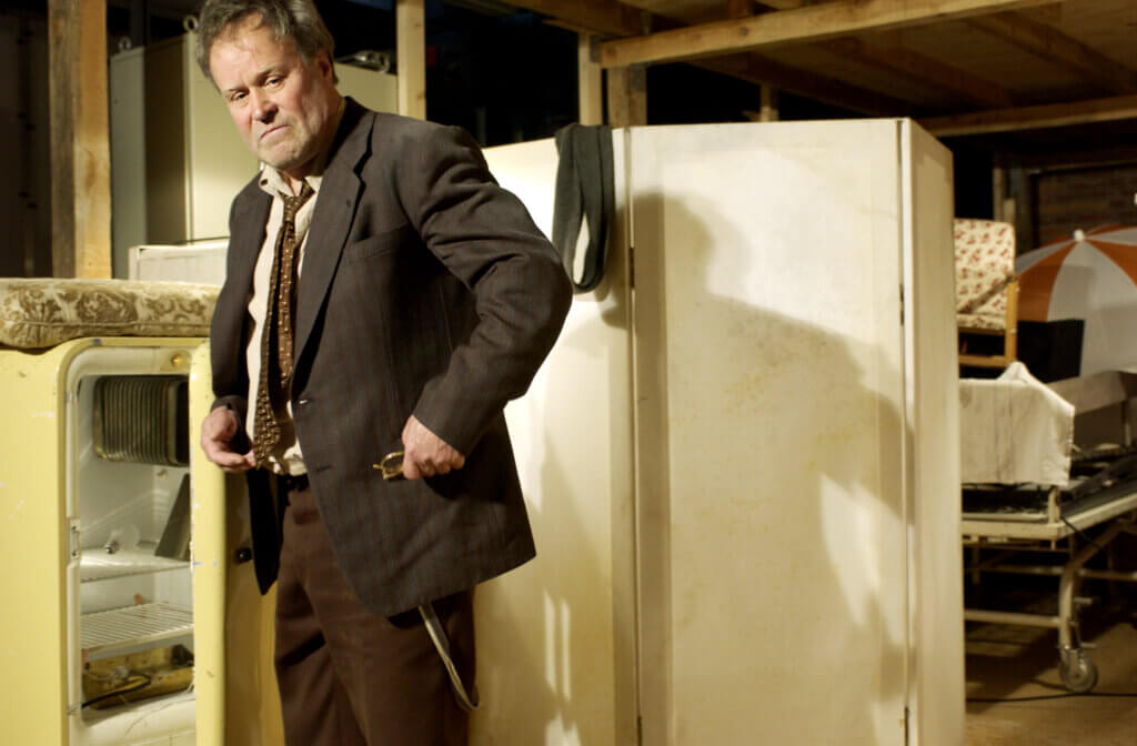 Aufführungsfoto von Bartleby am Thalia Theater Hamburg. Ein Mann im Anzug steht vor einem Paravent und steckt sich seine Brille in die Jackentasche.