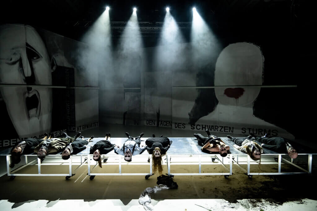 Aufführungsfoto von „Orestie“ von Robert Icke am Theater Vorpommern. Auf der Bühne liegen nebeneinander neu Menschen.
