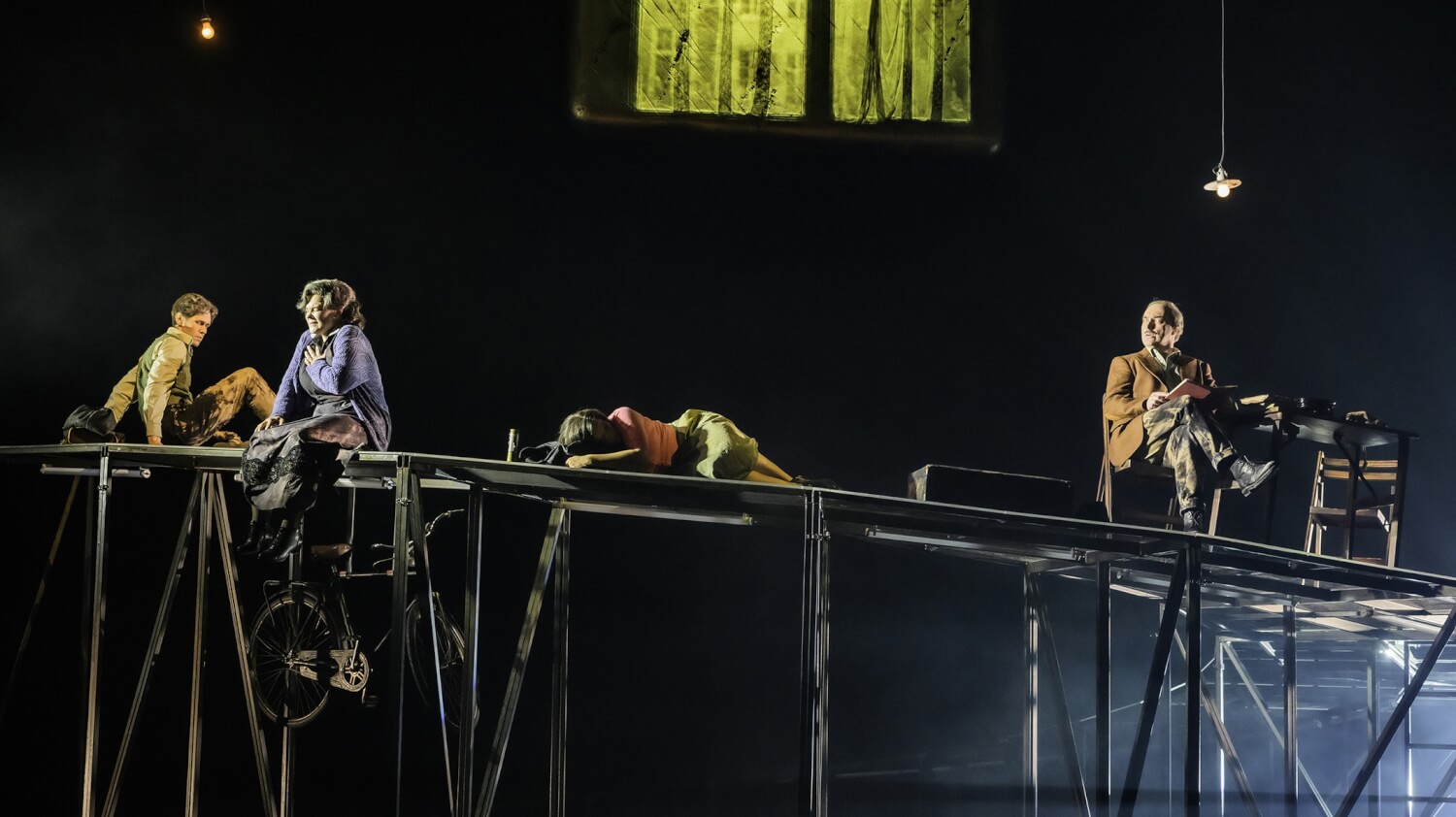 Aufführungsfoto von „Peter van Pels“ am Theater Osnabrück. Auf einem Metallkonstrukt sitzen und liegen vier Personen in schummrigen Licht.