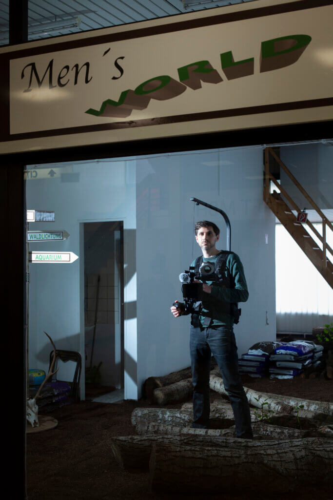 Videographer Lukas Raber mit seiner Kamera in einem Bühnenbild stehend.