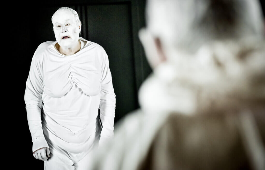 Aufführungsfoto von „Zauberberg“ am Deutschen Theater Berlin. Ein älterer Mann ganz in weiß gekleidet und weiß geschminkt.