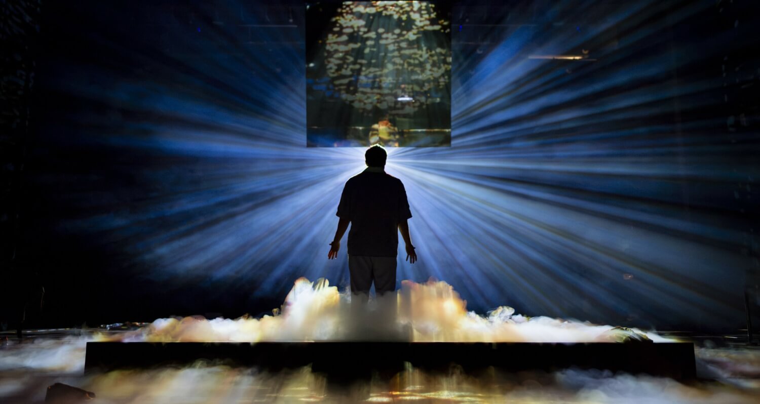 „Haus zur Sonne“ nach dem Roman von Thomas Melle am Schauspiel Hannover. Nebenschwaden am Boden, in einem dunklen Raum, der nur von hinten durch einen strahlendes Licht durchbrochen wird. Davor steht ein Mann im Gegenlicht.