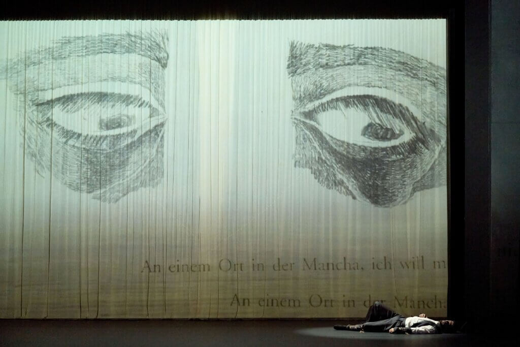 „Don Quixote“ von Jorge Pérez Martínez am Landestheater Eisenach. Ein mit Bleistift gezeichnete Augen, die einen Mann anschauen, der rechts auf dem Bühnenboden liegt.