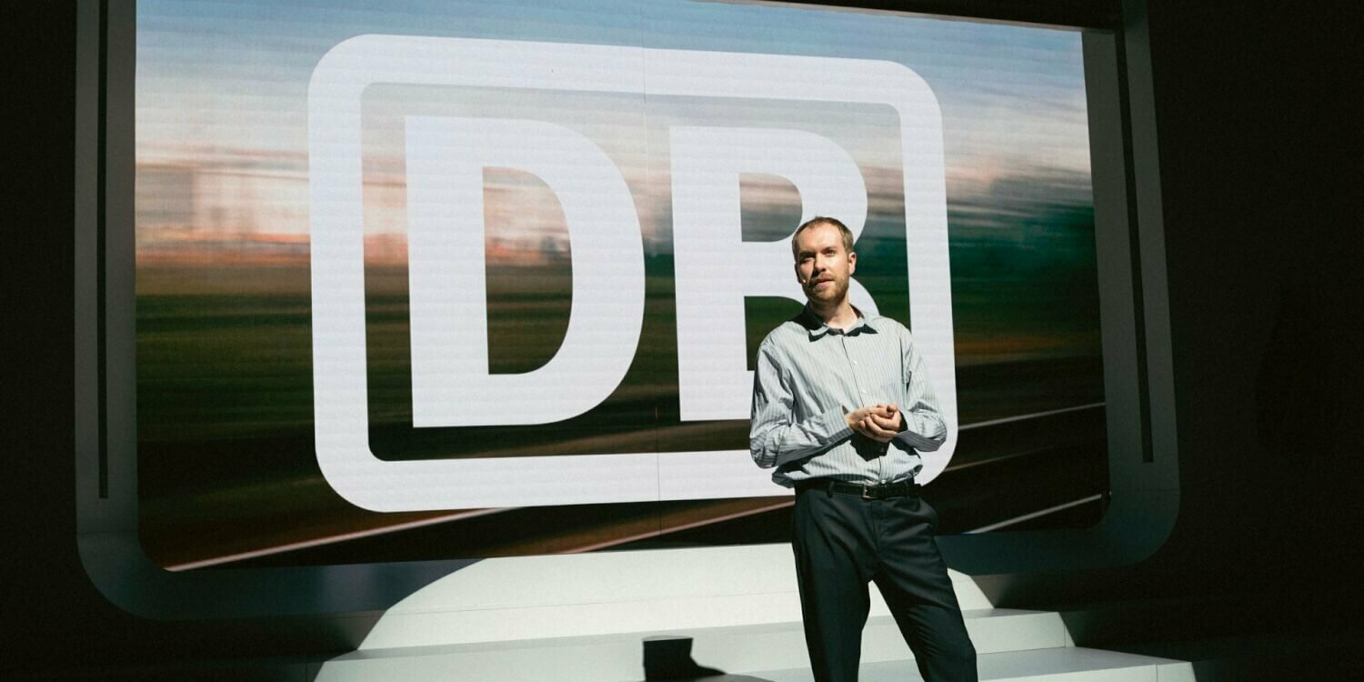 eine Person referiert auf einer Bühne vor dem Deutsche Bahn Logo