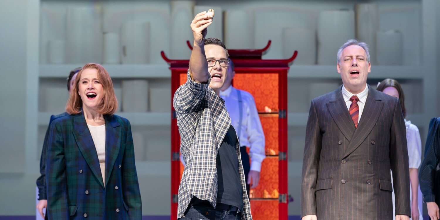 „Der Hase mit den Bernsteinaugen“ an der Oper Leipzig. Ein Mann in der Mitte hält eine kleine Hasenfigur hoch. Links neben ihm steht eine Frau und rechts ein Mann.